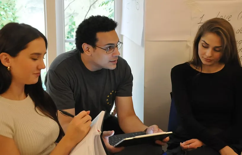 Three participants in a small-group discussion during a workshop, one taking notes