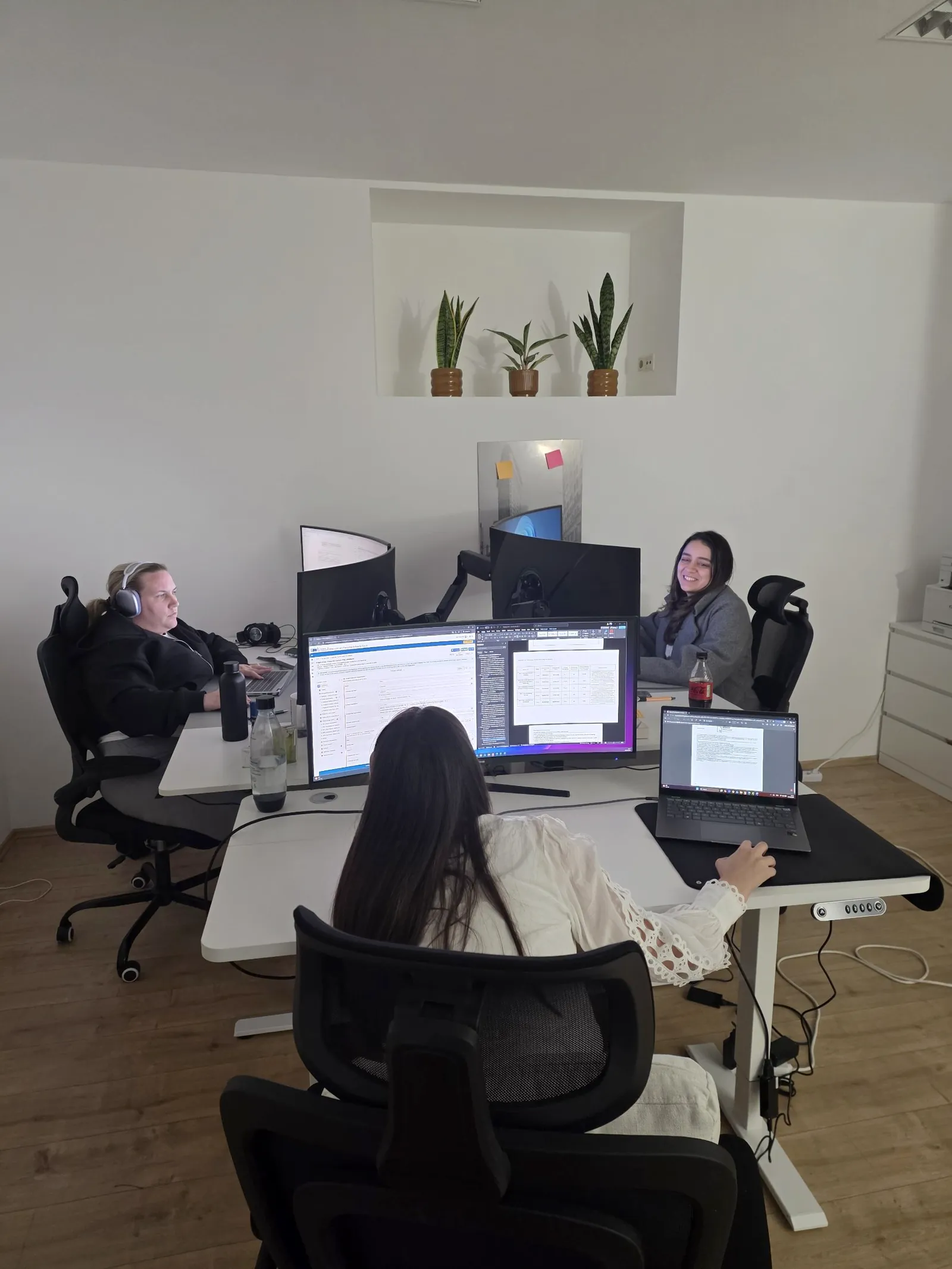 Three team members working at desks with large monitors and laptops