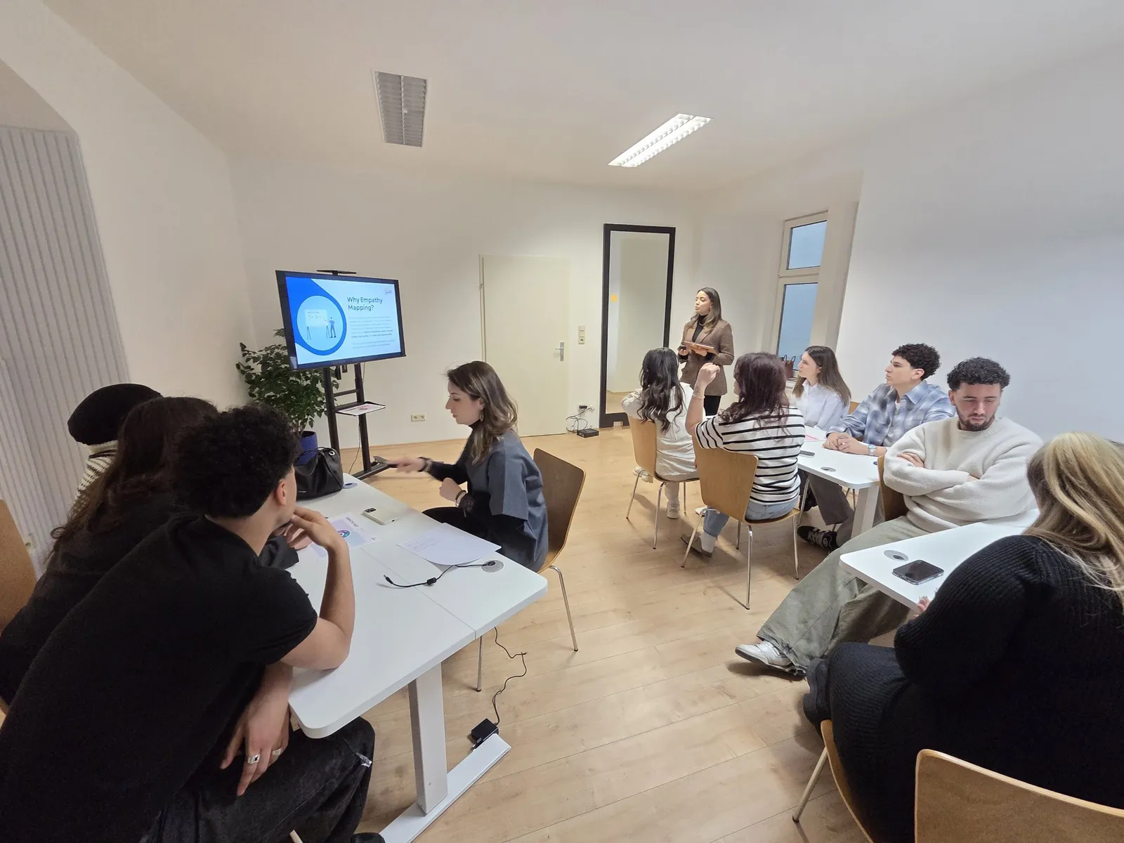 A trainer presents a slide on empathy mapping while young people work in groups at white tables